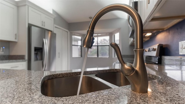 interior details with white cabinets, dark stone countertops, and stainless steel refrigerator with ice dispenser