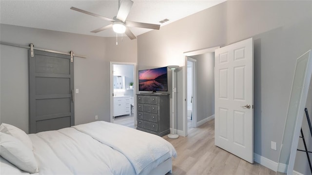 bedroom featuring ceiling fan, a barn door, light hardwood / wood-style flooring, ensuite bathroom, and lofted ceiling