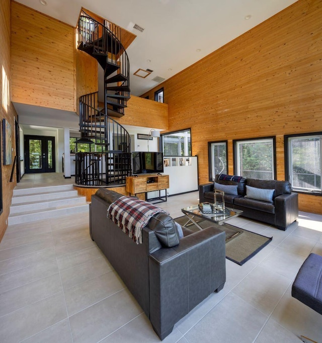 tiled living area with a wealth of natural light, wood walls, stairs, and a towering ceiling