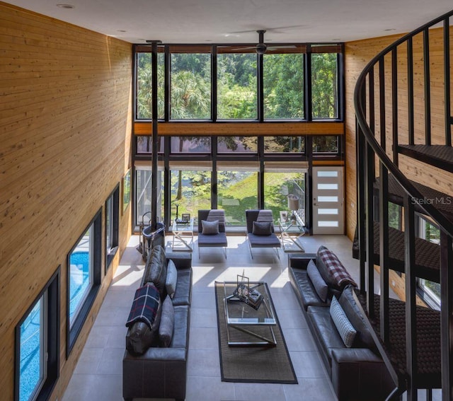 living room featuring floor to ceiling windows, wood walls, a ceiling fan, and a towering ceiling