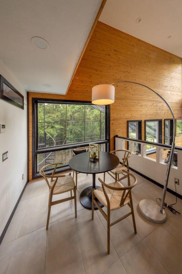 dining area with light tile patterned floors, wood walls, a high ceiling, and baseboards