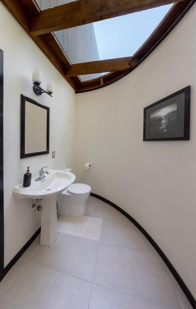 half bath with baseboards, toilet, a skylight, and tile patterned flooring