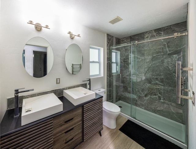 bathroom featuring a marble finish shower, visible vents, toilet, wood finished floors, and a sink