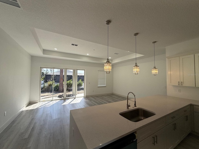 kitchen featuring white cabinetry, sink, hanging light fixtures, a raised ceiling, and light hardwood / wood-style flooring