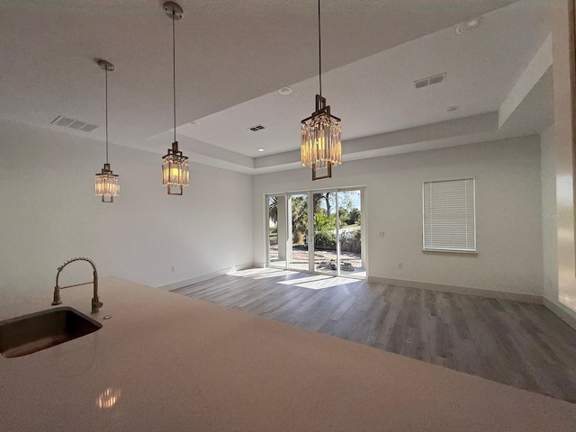 kitchen with hardwood / wood-style floors, a raised ceiling, sink, hanging light fixtures, and a chandelier