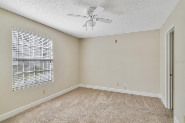 spare room featuring a ceiling fan, light carpet, a textured ceiling, and baseboards