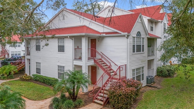 view of front of home with central AC, a shingled roof, stairway, and a front yard