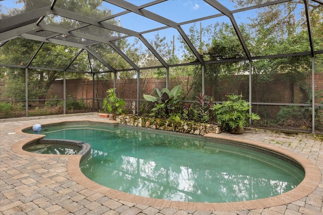 view of pool with glass enclosure, an in ground hot tub, and a patio