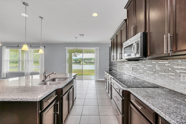 kitchen with appliances with stainless steel finishes, light stone counters, a kitchen island with sink, and sink