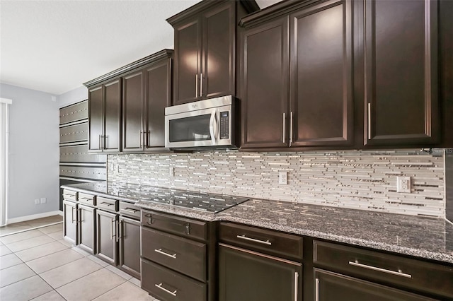 kitchen featuring dark brown cabinets, light tile patterned floors, dark stone counters, and black stovetop