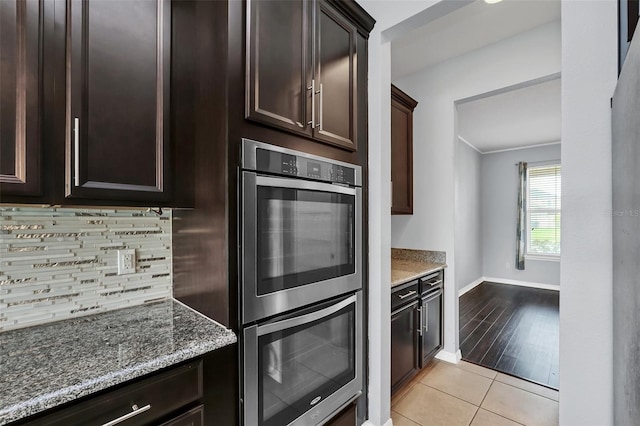 kitchen with light hardwood / wood-style flooring, dark brown cabinetry, tasteful backsplash, stone countertops, and stainless steel double oven