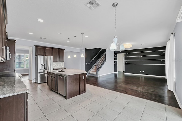 kitchen with dark brown cabinetry, stainless steel appliances, a kitchen island with sink, light hardwood / wood-style flooring, and hanging light fixtures