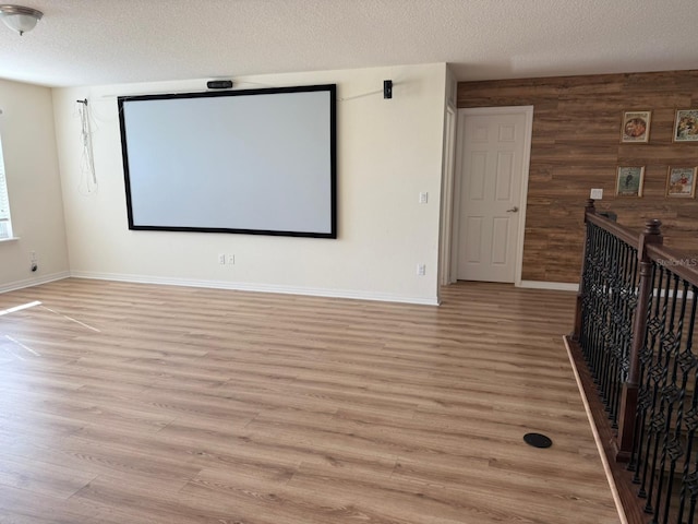 home theater room with a textured ceiling, light wood-type flooring, and wood walls