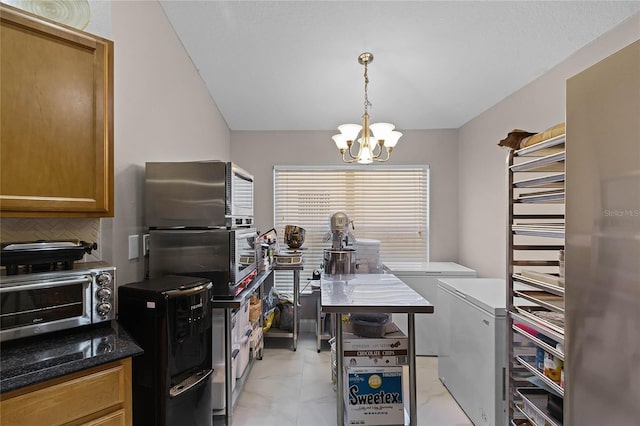 kitchen featuring dark stone counters, a notable chandelier, fridge, pendant lighting, and decorative backsplash