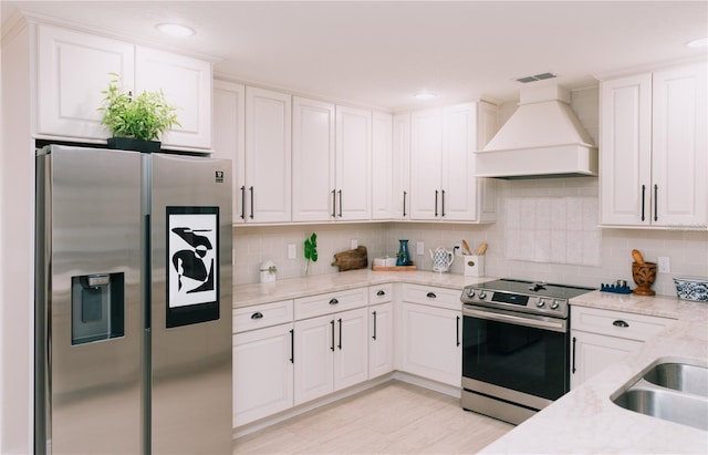 kitchen with stainless steel appliances, light stone countertops, white cabinetry, and custom exhaust hood