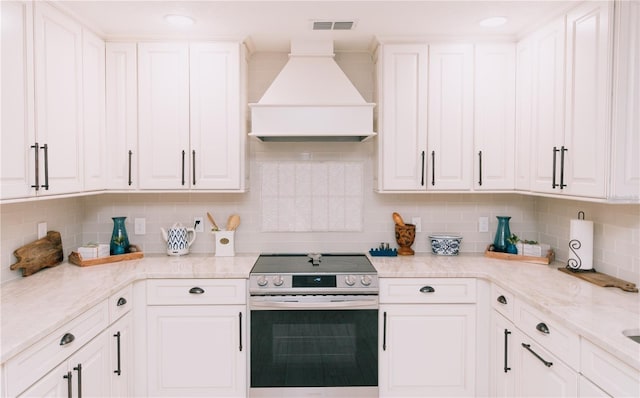 kitchen featuring white cabinetry, tasteful backsplash, light stone countertops, stainless steel range with electric cooktop, and premium range hood