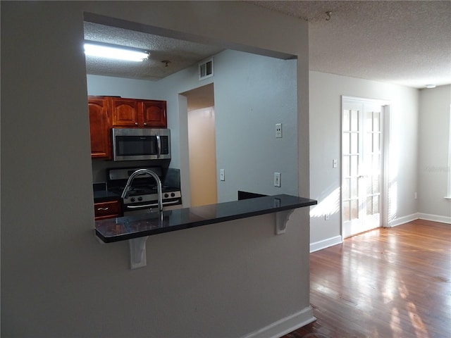 kitchen featuring light hardwood / wood-style flooring, kitchen peninsula, a textured ceiling, a breakfast bar, and appliances with stainless steel finishes