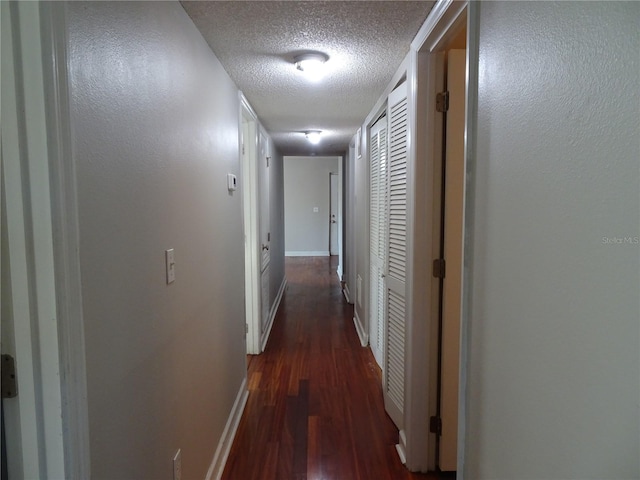 hall with a textured ceiling and dark wood-type flooring