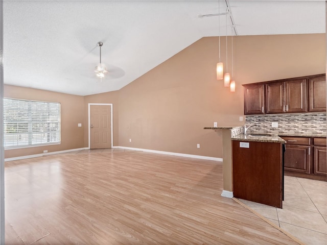 kitchen featuring high vaulted ceiling, pendant lighting, light stone countertops, and light hardwood / wood-style flooring