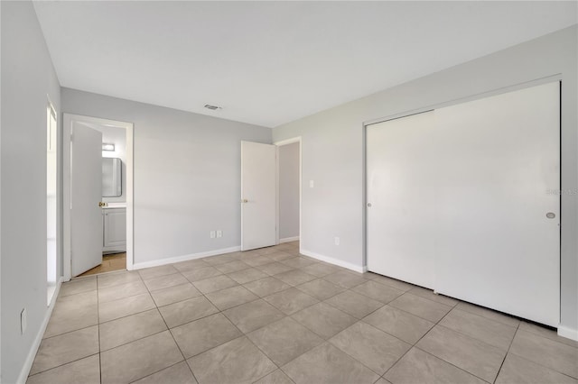 unfurnished bedroom with ensuite bathroom, light tile patterned floors, and a closet