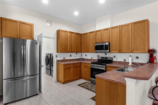 kitchen with tasteful backsplash, appliances with stainless steel finishes, sink, washing machine and clothes dryer, and kitchen peninsula