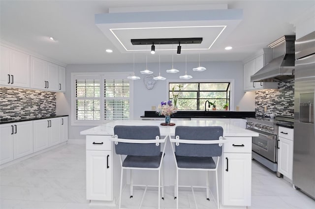 kitchen with white cabinets, stainless steel appliances, decorative light fixtures, and wall chimney range hood