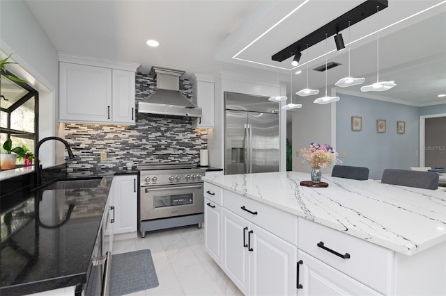 kitchen with wall chimney exhaust hood, white cabinetry, high end appliances, and sink