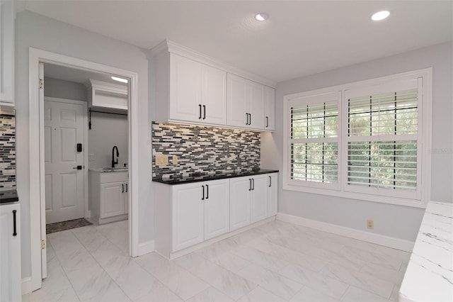 kitchen with white cabinets, sink, dark stone countertops, and backsplash