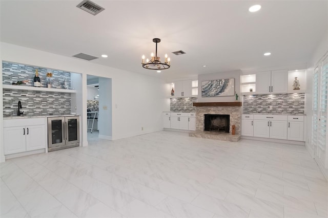 unfurnished living room featuring a stone fireplace, beverage cooler, wet bar, and an inviting chandelier