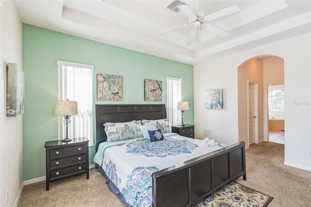 bedroom featuring a tray ceiling, light carpet, ceiling fan, and ensuite bathroom