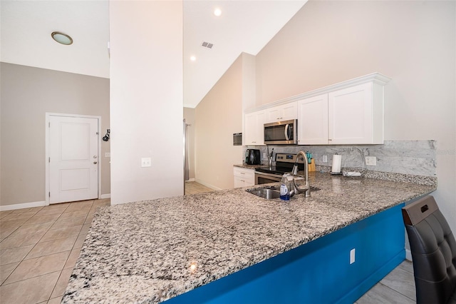 kitchen featuring stainless steel appliances, tasteful backsplash, high vaulted ceiling, stone counters, and white cabinets