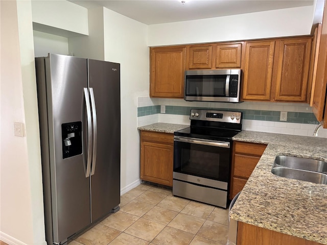 kitchen with tasteful backsplash, light stone countertops, appliances with stainless steel finishes, and light tile patterned floors