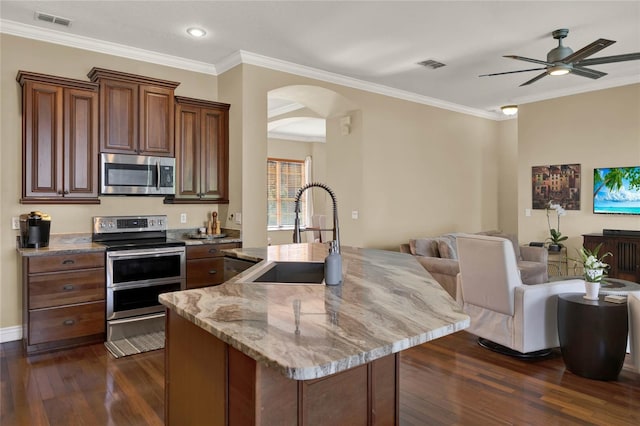 kitchen with a center island with sink, ornamental molding, appliances with stainless steel finishes, sink, and dark wood-type flooring