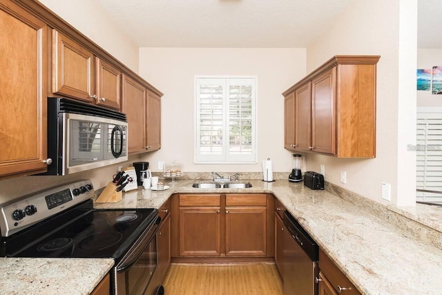 kitchen featuring light wood-type flooring, stainless steel appliances, sink, and light stone counters