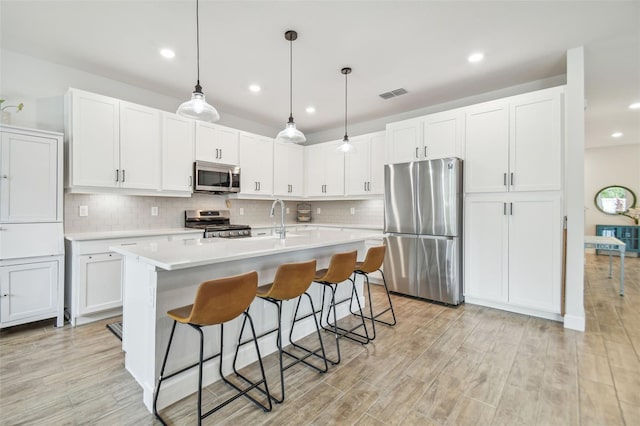 kitchen featuring stainless steel appliances, tasteful backsplash, hanging light fixtures, light hardwood / wood-style flooring, and white cabinets