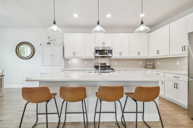 kitchen with appliances with stainless steel finishes, hanging light fixtures, decorative backsplash, white cabinets, and a kitchen island with sink