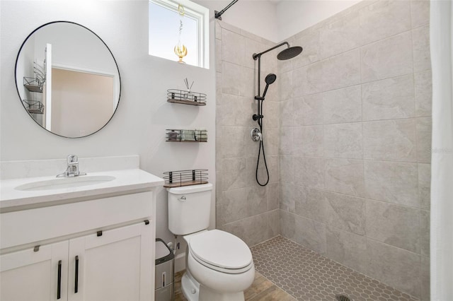 bathroom with toilet, vanity, wood-type flooring, and a tile shower