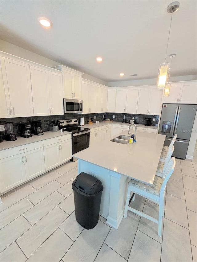 kitchen featuring a center island with sink, decorative backsplash, a breakfast bar area, pendant lighting, and appliances with stainless steel finishes