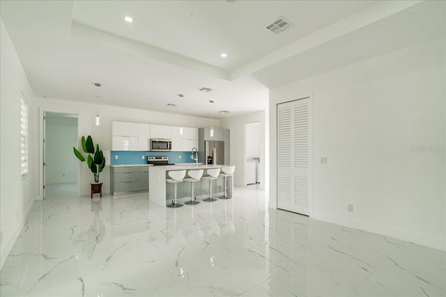 kitchen with a center island with sink, white cabinetry, appliances with stainless steel finishes, tasteful backsplash, and hanging light fixtures