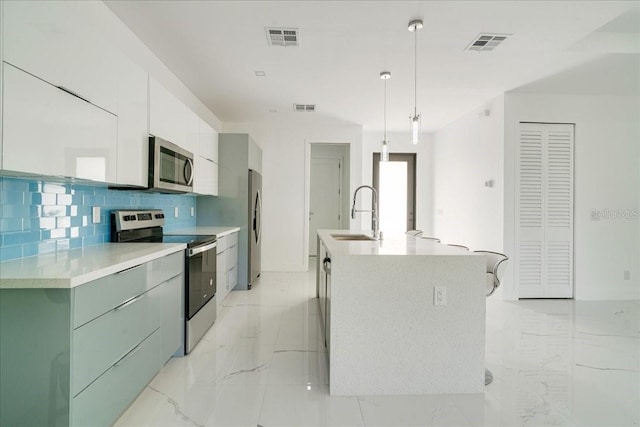 kitchen featuring stainless steel appliances, sink, hanging light fixtures, a kitchen island with sink, and decorative backsplash