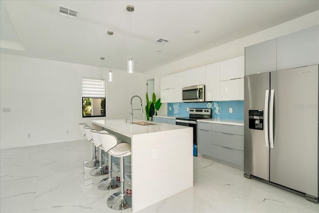 kitchen with sink, appliances with stainless steel finishes, tasteful backsplash, a kitchen island with sink, and pendant lighting