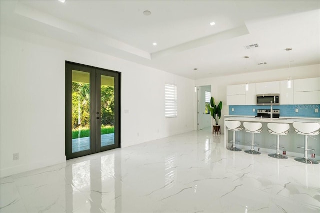 kitchen with tasteful backsplash, french doors, appliances with stainless steel finishes, a kitchen breakfast bar, and white cabinets