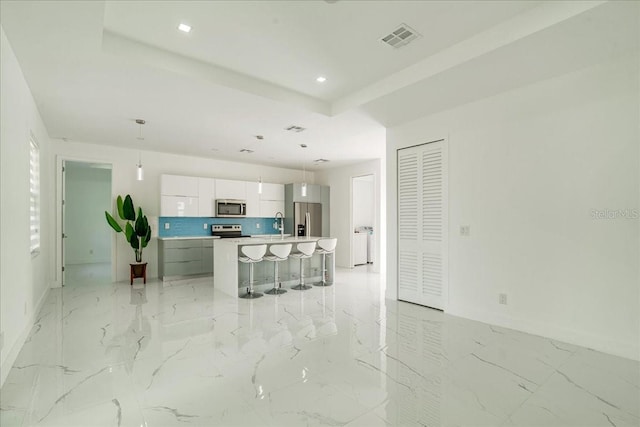 kitchen with an island with sink, backsplash, pendant lighting, appliances with stainless steel finishes, and white cabinetry