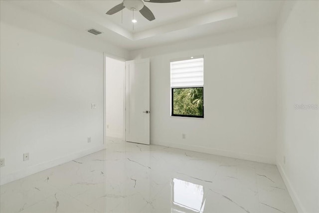 empty room with ceiling fan and a tray ceiling