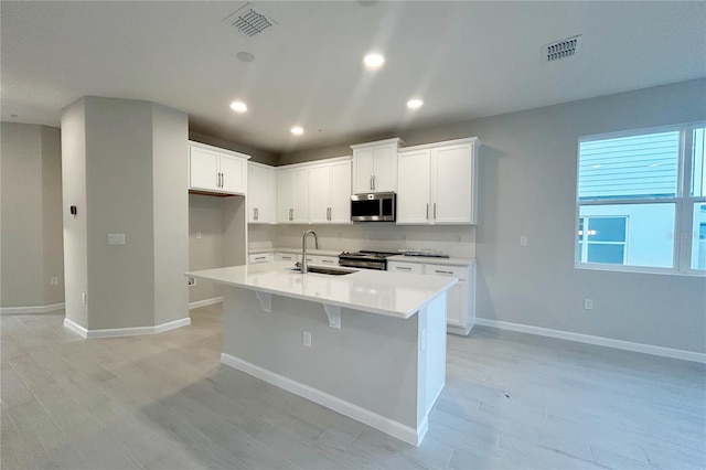 kitchen with appliances with stainless steel finishes, a kitchen island with sink, sink, light hardwood / wood-style floors, and white cabinetry