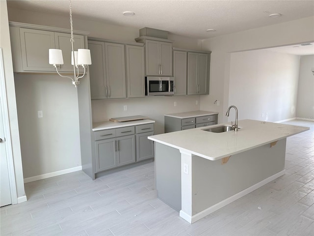 kitchen with gray cabinetry, sink, and an island with sink