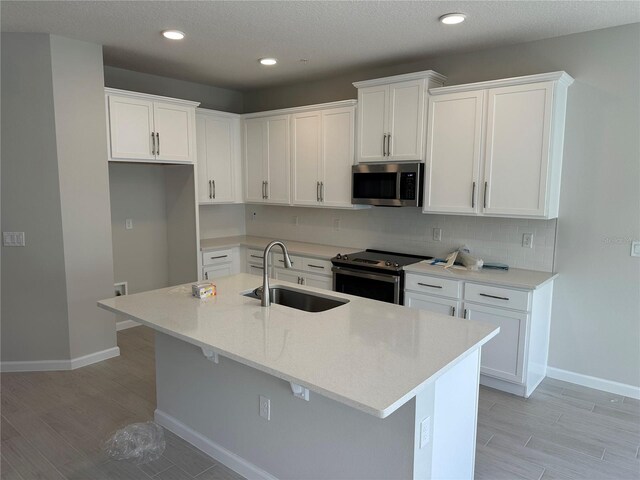 kitchen with stainless steel appliances, white cabinetry, a center island with sink, and sink