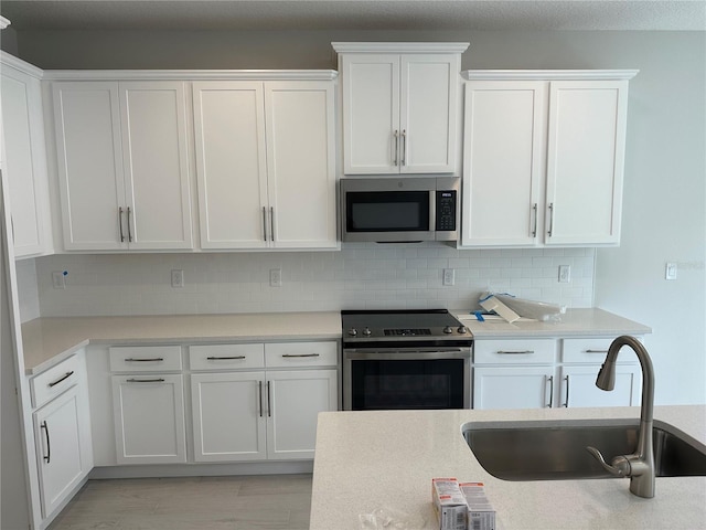 kitchen featuring appliances with stainless steel finishes, light wood-type flooring, backsplash, sink, and white cabinetry