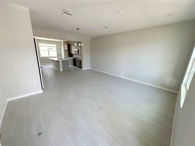 unfurnished living room featuring a textured ceiling, light hardwood / wood-style floors, and sink