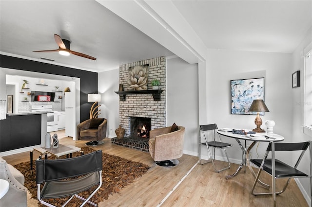 living room featuring a brick fireplace, ceiling fan, light wood-type flooring, and crown molding